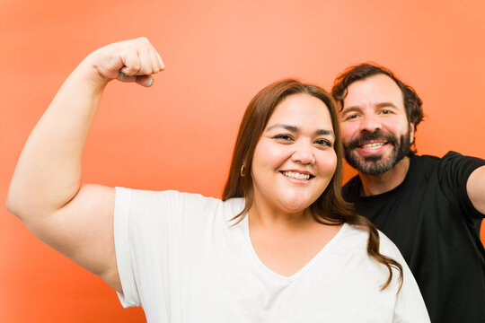 Woman flexing bicep showing strength and body positivity with a smiling man in a couple portrait
