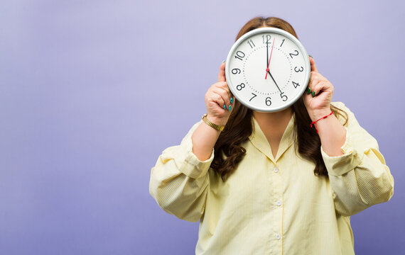 Woman holding a clock covering her face, illustrating time management, meeting deadlines, and busy schedules