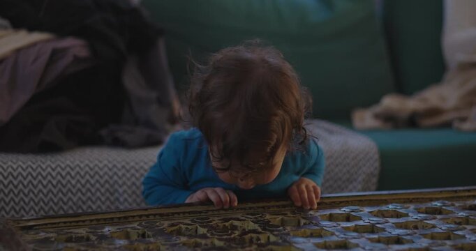 Toddler stands supported beside perforated coffee table at home, watching a small object fall through holes while exploring cause and effect, balance and curiosity