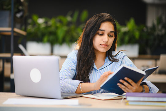 Indian student studying book, using laptop for education