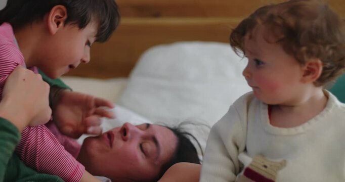 Older brother pushes toddler away on bedroom bed to keep mother&rsquo;s attention, revealing sibling rivalry, jealousy, emotional boundaries and authentic family dynamics