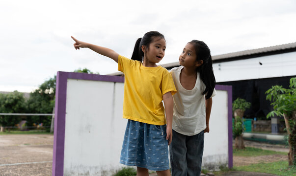 Happy children standing outdoors at a school playground, pointing into the distance and sharing a moment of curiosity. Friendship, communication, learning, imagination, teamwork and joyful childhood.