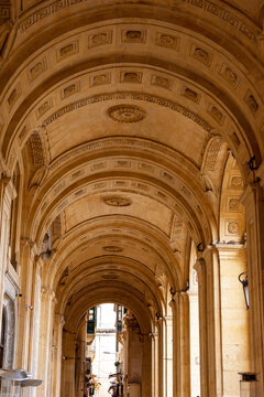 Perspective view of a grand limestone arcade with decorative coffered ceilings and Greek key patterns in historic Valletta, Malta.