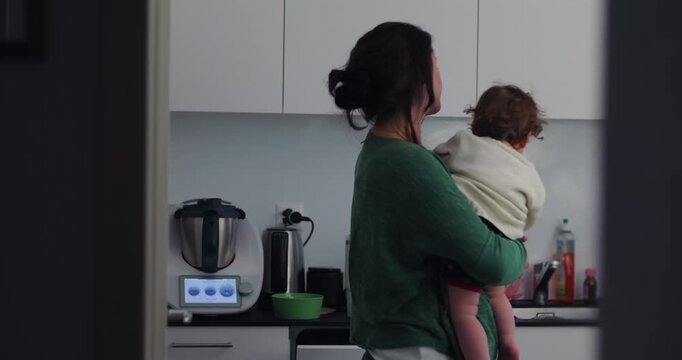 Mother holds toddler close and kisses him in home kitchen, expressing deep maternal affection, protective love, secure attachment and authentic everyday connection