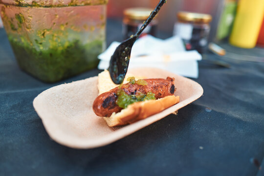 Grilled sausage in a bun with relish being spooned on at a food festival