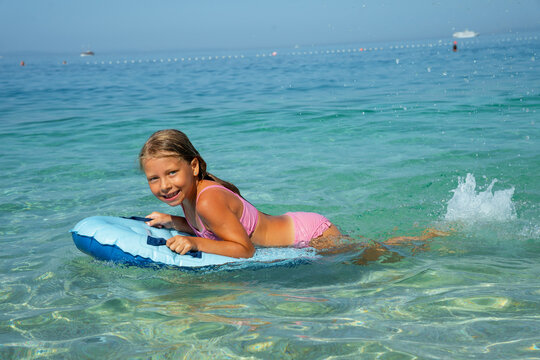 Girl in pink bikini on blue inflatable board in clear turquoise sea water.