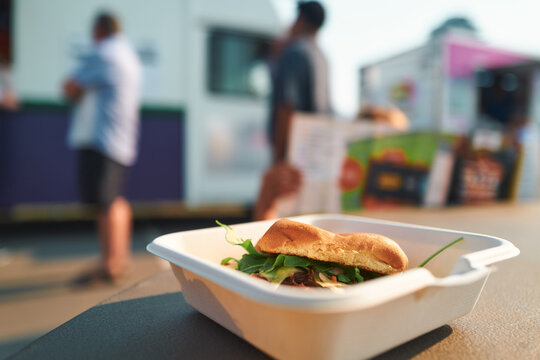 Pulled pork sandwich on a table with food trucks and crowds behind