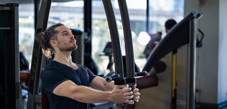 Caucasian man with strong and muscular body training on chest press machine in gym for muscle building and weight lifting practice with back light