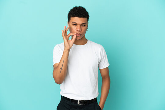 Young African American man isolated on blue background showing a sign of silence gesture
