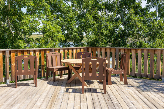 Wooden Patio Deck with Outdoor Table and Chairs Overlooking Trees and Lakeshore.