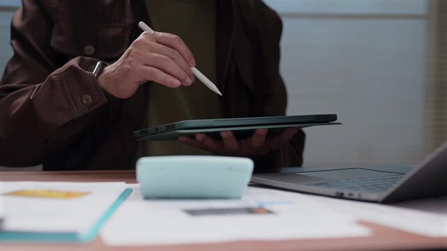 Man sits desk holding pad stylus checking finance sheet calculator laptop screen staff planning budget tasks firm career boss work team job role duty goal target scheme action.