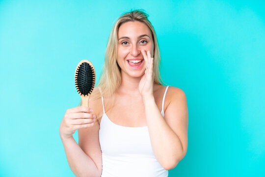 Young caucasian woman with hair comb isolated on blue background shouting with mouth wide open