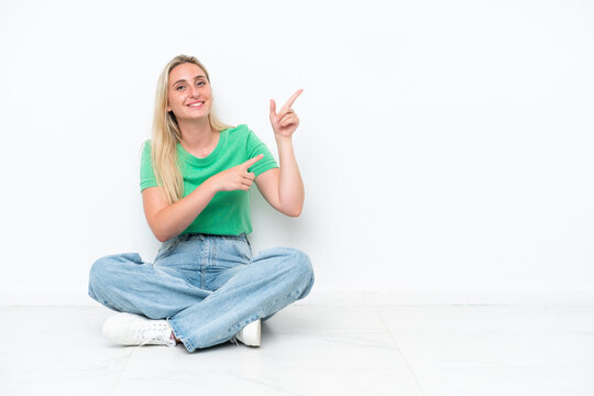 Young caucasian woman sitting on the floor isolated on white background pointing finger to the side and presenting a product