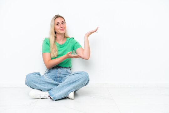 Young caucasian woman sitting on the floor isolated on white background extending hands to the side for inviting to come