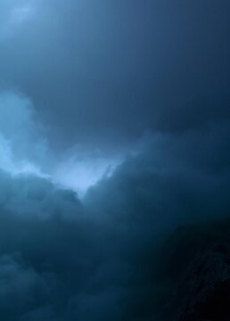 Photograph of a cloudy sky over a mountain range. the sky is a deep blue color and the clouds are white and fluffy.