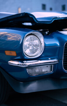 Close-up detail of the front headlight and bumper of a classic vintage blue car with the hood open.