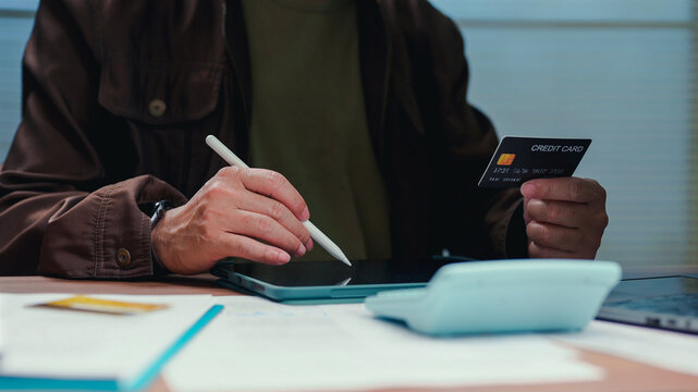 Person holding card stylus pad calculating budget costs shopping online paying banking expenses money ledger investment funds earnings economy commerce trades revenue profits asset debit loans cash.