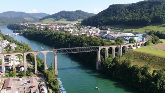 Eglisau, Switzerland - September 09, 2021: Aerial drone flight over the historic Eglisau railway bridge crossing the Rhine River in Switzerland, surrounded by green landscape on a sunny summer day.