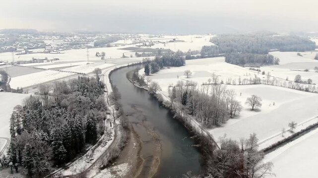 Aerial drone flight over the Reuss River near Sins, Switzerland, showing a snow covered winter landscape with railway line, river and rural countryside.