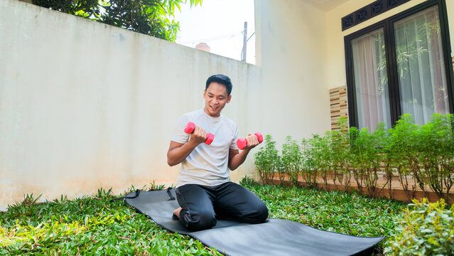 Man Doing Home Fitness Workout With Dumbbells On Yoga Mat In Garden Patio