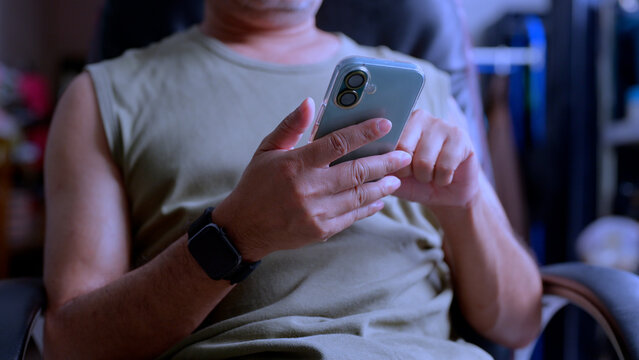 Adult man holds phone scrolling display, checks own mobile device messaging app, browses social feed, communicates remotely, executes digital business transaction, sits office chair, reviews daily.