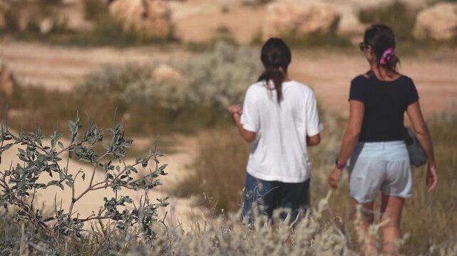 Mother and daughter walking hand in hand through Western Australia landscape, back view at sunset