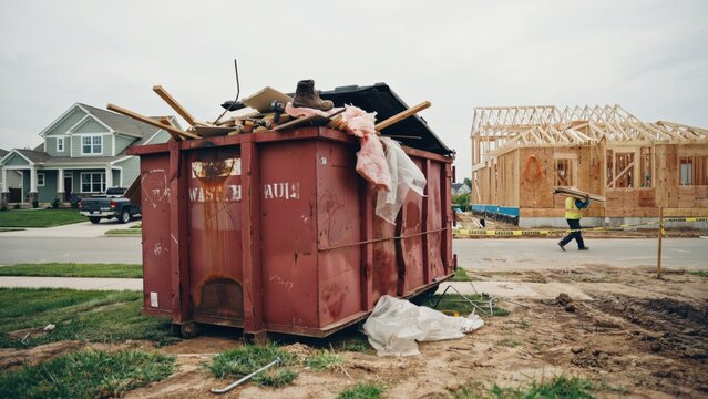Construction site with a large red dumpster and a worker carrying wood