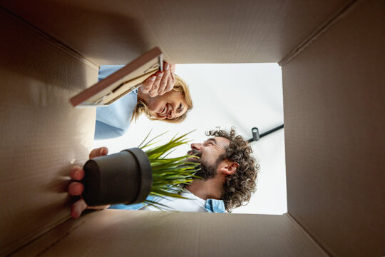 Couple looking at a book while unpacking a cardboard box in a room with natural light