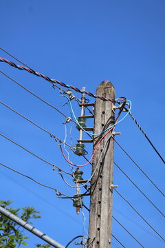 Weathered concrete utility pole with multiple electrical wires and glass insulators against a clear blue sky