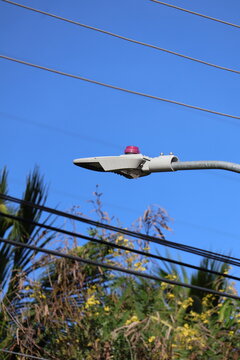 Modern street lamp with a red indicator light against a clear blue sky and overhead wires
