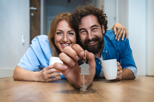 Couple holds keys to new home while enjoying drinks indoors on a wooden floor