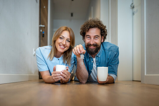 Couple celebrates new home in hallway while holding mugs and keys