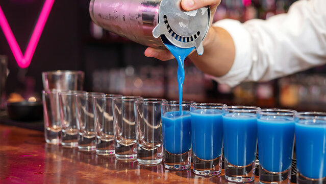 Professional bartender making blue cocktail shots for customers at nightclub