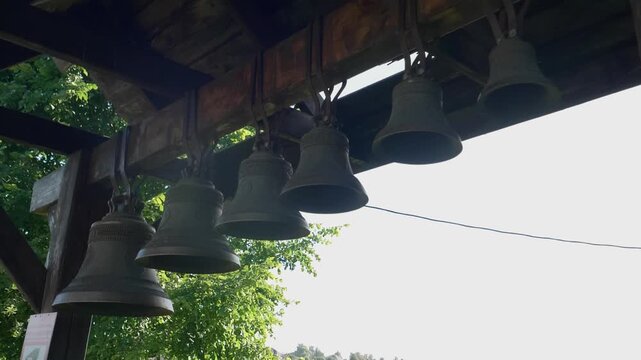 Row of traditional bronze church bells hanging under a wooden belfry roof outdoors