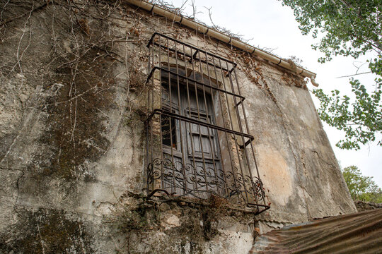 Vintage wooden shutter window in a rusted iron cage on a Spanish building surrounded by growth