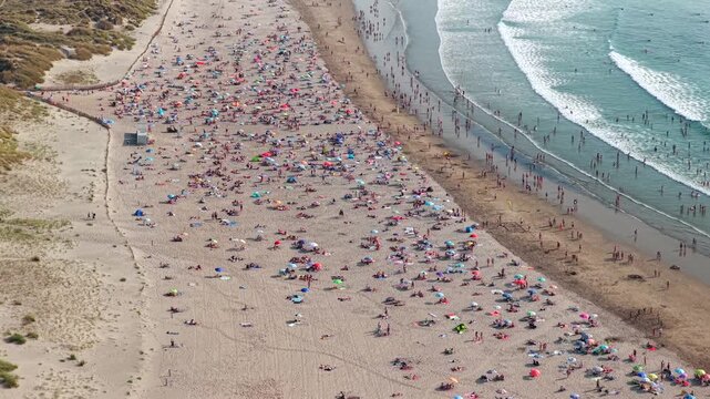 Aerial High-Angle View of Crowded Sunbathers and Swimmers Packed on a Golden Sand Beach in Northern Spain During a Summer Heatwave