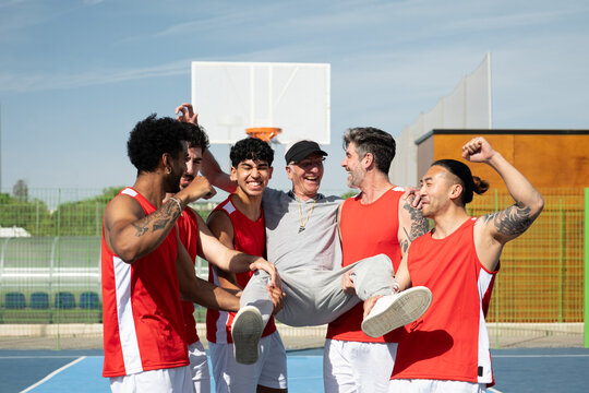 Basketball players celebrating a win and lifting their coach on the court