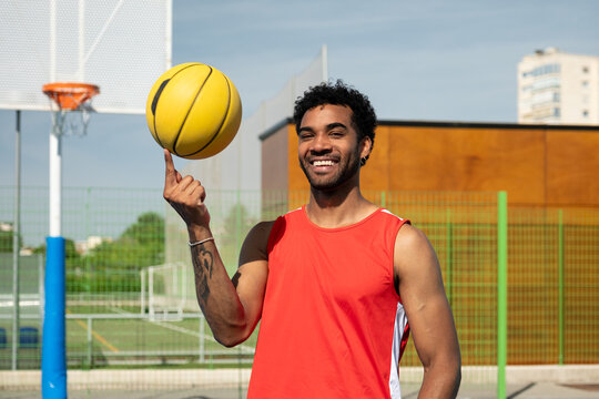 Smiling athlete spinning a yellow basketball on his finger enjoying a sport moment
