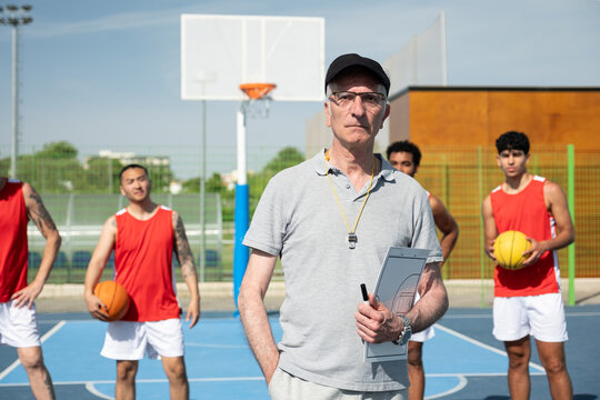 Coach holding clipboard and pen, watching his diverse team on a sunny outdoor court