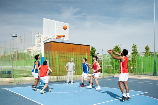 Men are playing basketball together on an outdoor urban court on a sunny day