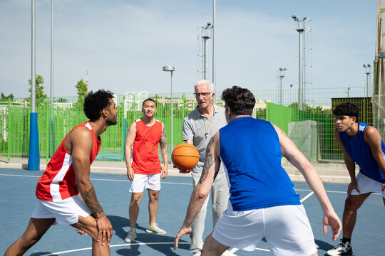 Referee holding basketball while players preparing to start a game outdoors