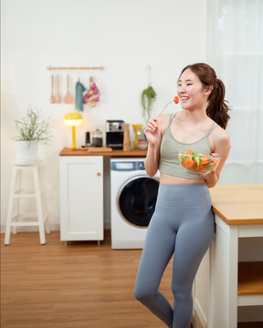 Woman Enjoys Salad in a Kitchen While Standing Near a Counter and Smiling