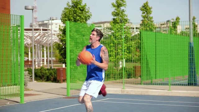 Athletic man with tattoos dribbling a ball and scoring on an outdoor court
