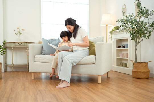 Girl Sits on a Couch While Mom Reads a Story in a Bright Living Room