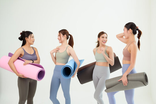 Four Women in a Yoga Class Prepare With Mats and Props on a White Background