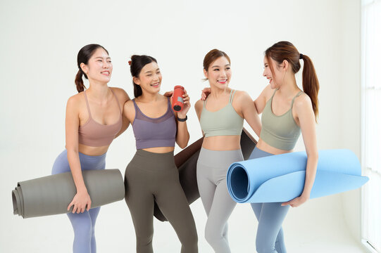 Four Women in a Yoga Class Prepare With Mats and Props on a White Background