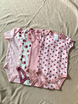 Collection of cute newborn baby clothes rompers and onesies arranged flat lay on soft fabric background