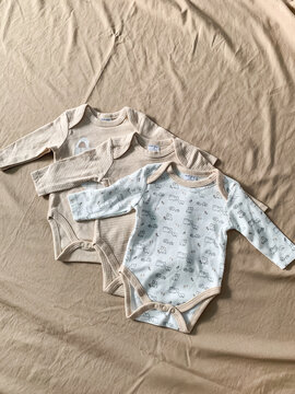 Medan, Indonesia - September 12, 2023: Collection of cute newborn baby clothes rompers and onesies arranged flat lay on soft fabric background
