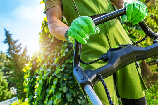 Gardener working with a lawn mower in a green backyard during the day
