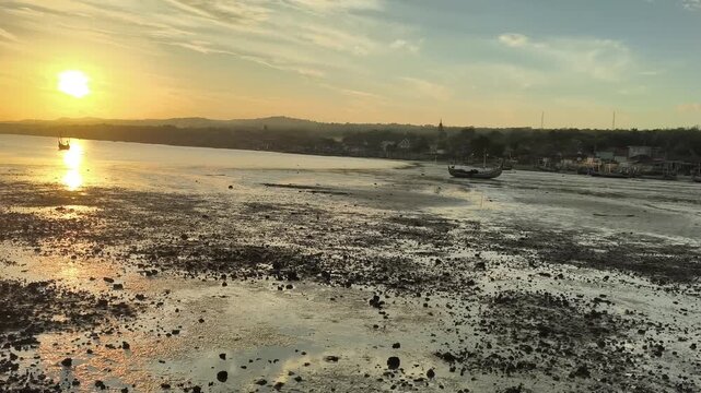 Traditional boats resting on tropical mudflats at low tide during golden hour sunset reflection